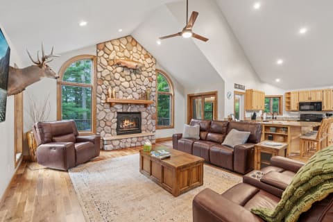 Cozy living room with stone fireplace, leather sofas, and modern kitchen.