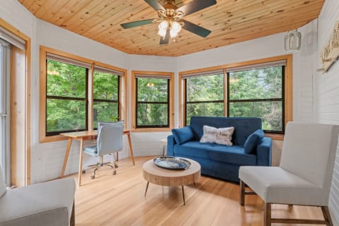 A bright sunroom with a blue sofa, wooden ceiling, and desk with chair.