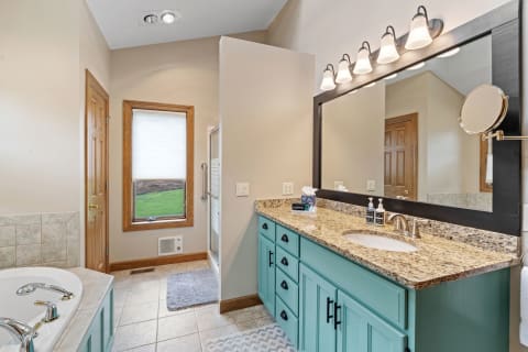 A well-designed bathroom featuring a turquoise cabinet, granite countertop, and large mirror with lighting.