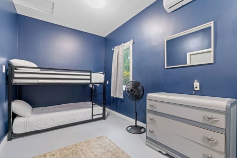 A cozy bedroom featuring a bunk bed, a dresser, and a fan against a navy blue wall.