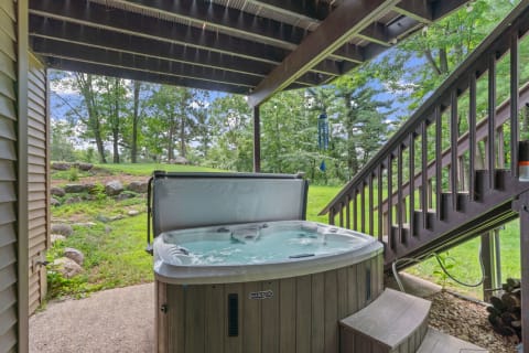 Hot tub under a wooden deck in a green outdoor setting.