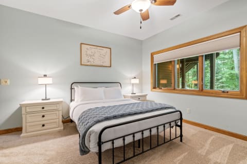 Cozy bedroom with a black metal bed, gray blanket, and a view of greenery outside.