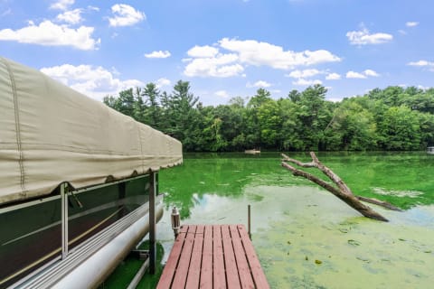 Lakeside scene featuring a dock and covered boat with green water and trees in the background.