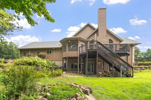 Two-story home with a spacious deck in a green environment, featuring a sunny sky and a well-kept lawn.