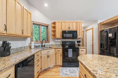 A spacious kitchen featuring warm wood cabinets, granite countertops, and modern black appliances.