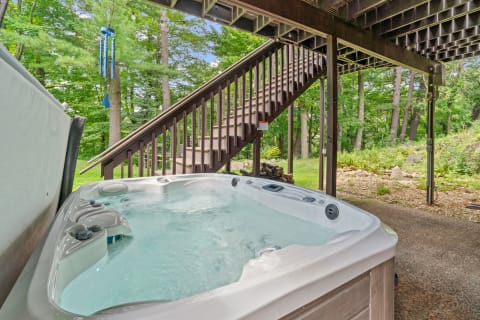 Hot tub under a wooden deck with surrounding greenery and a staircase.
