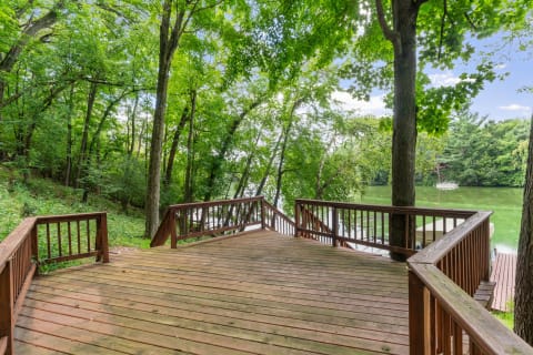 Wooden deck by a lake with lush trees and a sailboat moored in the background.