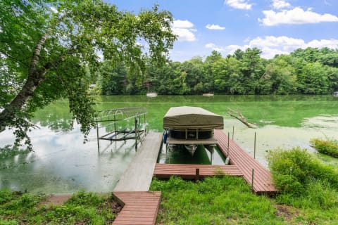 Serene lakeside view with a covered boat on a dock and lush surroundings.