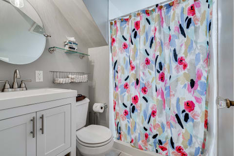 Colorful bathroom with floral shower curtain, white vanity, and neatly arranged towels.