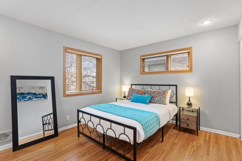 Modern bedroom featuring a black metal bed frame with colorful bedding, wooden windows, and a full-length mirror.
