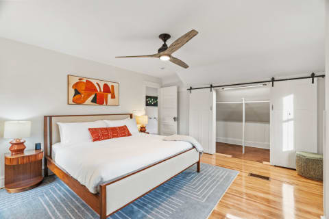 A stylish bedroom with a bed, artwork, wooden floors, and a closet.