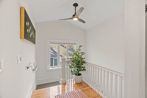 Elegant upstairs landing with hardwood floors, stylish ceiling fan, and green plant.