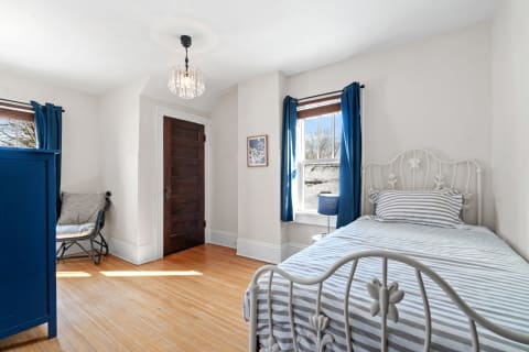 A cozy bedroom with a striped bed, blue curtains, and warm wooden flooring.