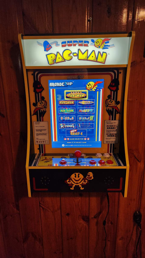 An arcade cabinet featuring 'Super Pac-Man' and other retro games mounted on a wooden wall.