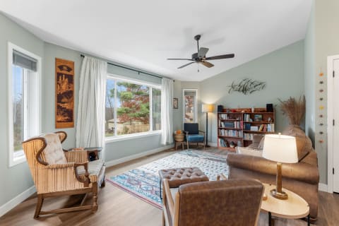 A cozy living room with light green walls, large windows, and comfortable furniture.