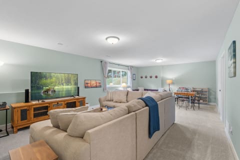 A spacious and inviting basement living room featuring a beige sectional sofa, a large TV, and a cozy dining area.