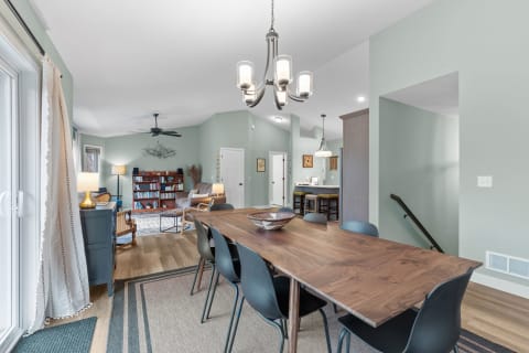 Open dining space with a wooden table and black chairs, leading into a living area with a bookshelf.