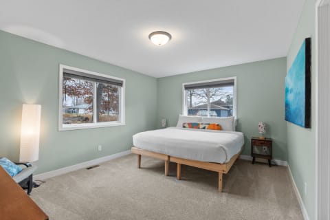 A peaceful bedroom with light green walls, a wooden bed, and large windows.