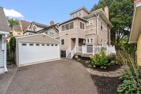 A two-story residential home with a wooden deck, surrounded by greenery and a garage.