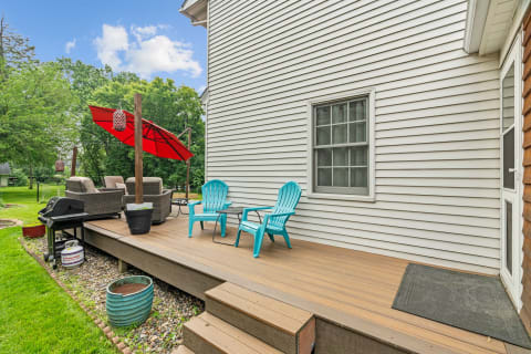 Outdoor deck featuring turquoise chairs, a grill, and a red umbrella among greenery.