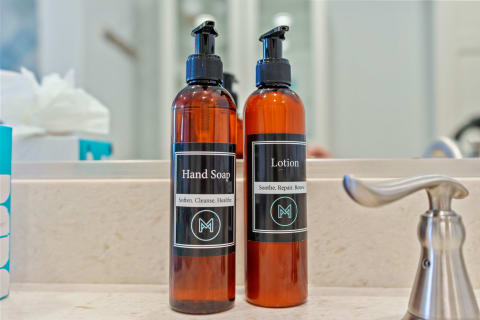 Two amber bottles labeled 'Hand Soap' and 'Lotion' on a light stone countertop.