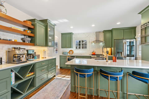 Modern kitchen featuring green cabinets, a white countertop, and stylish bar stools.