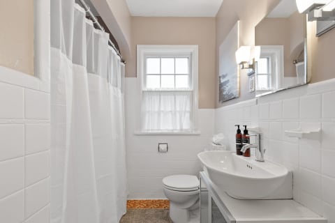 A modern bathroom featuring a white shower curtain, sink, and window.