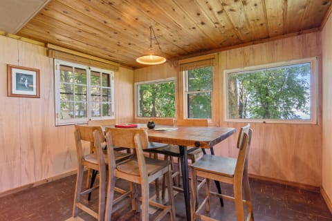 Interior of a wooden dining area with a table and chairs, surrounded by windows.