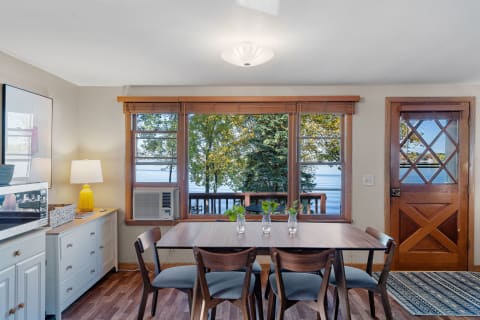 Dining area featuring a wooden table, chairs, and a view of trees and water through large windows.