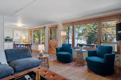Cozy living room with turquoise chairs and large windows overlooking nature.
