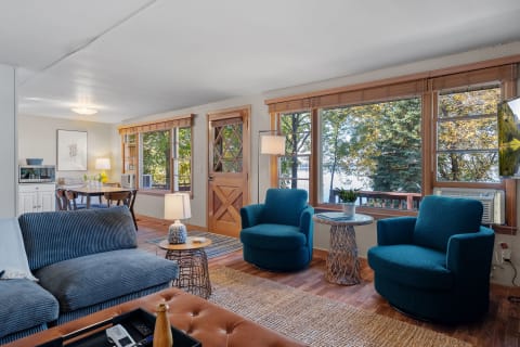 Living room with blue sofa, turquoise chairs, and a view of the lake through large windows.