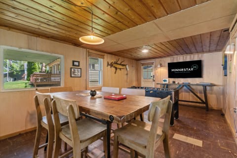 A rustic interior with a wooden dining table and foosball table, showcasing warm wood tones and natural light.