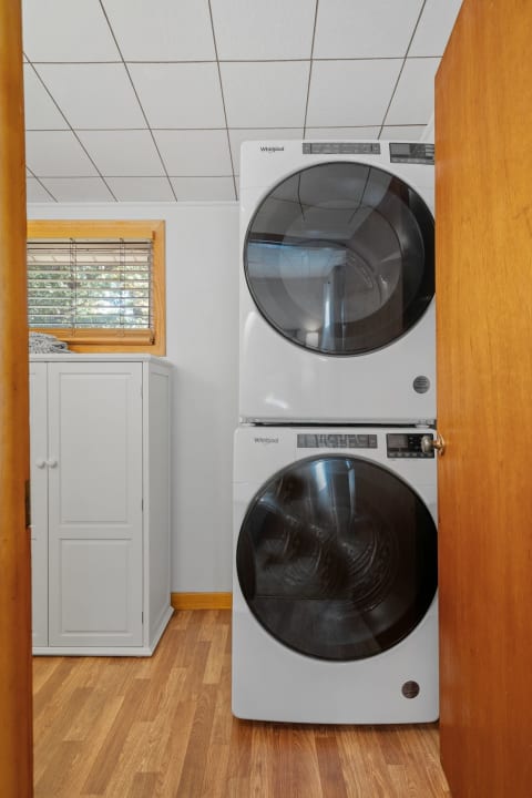 Compact laundry area with a stacked Whirlpool washer and dryer, white cabinet, and wooden flooring.