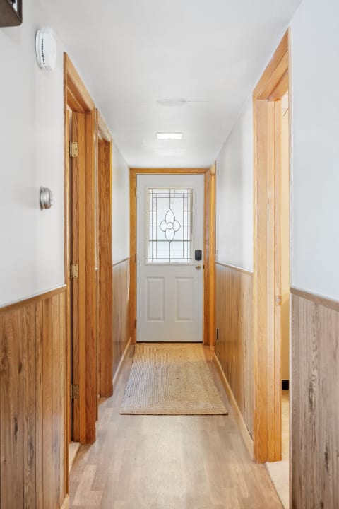 A light-filled hallway with wooden doors, a rug, and a glass door at the end.