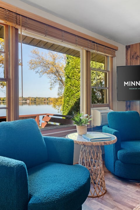 Cozy living room with teal chairs overlooking a lake with autumn trees.