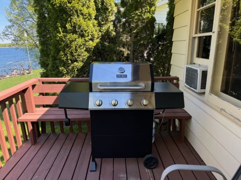 A black gas grill with stainless steel features on a wooden deck overlooking a lake.