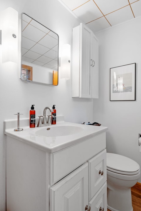 A bright modern bathroom with a white sink, two orange bottles of soap, and a rectangular mirror.