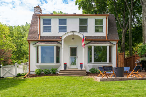 A two-story house with a shingle roof, bay windows, and a cozy patio.