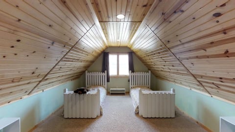 An attic room with two twin beds and a wooden ceiling.
