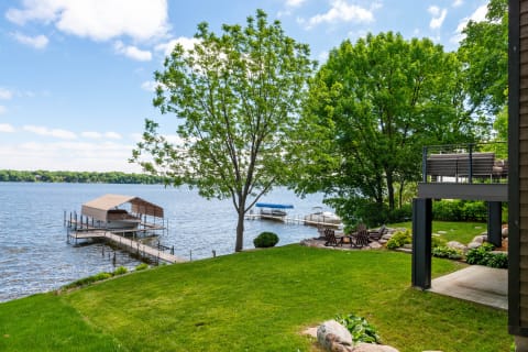 Lakeside scene featuring a dock, trees, and a green lawn.