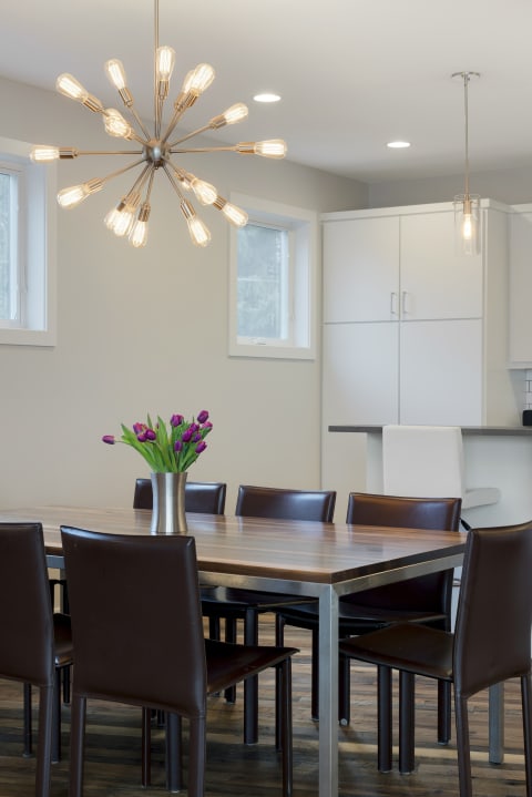 Modern dining area with a starburst chandelier, wooden table, and tulip vase.