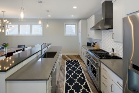 Modern kitchen with white cabinets, a countertop, and wood flooring, featuring a dining area in the background.