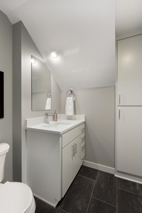 Modern bathroom with gray walls, white vanity, and dark tile flooring.