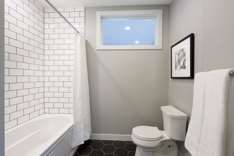 Modern bathroom featuring a white bathtub, subway tiles, gray walls, and hexagonal black tiles.