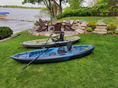 Two kayaks on grass by a lake, surrounded by trees and a wooden dock in the background.