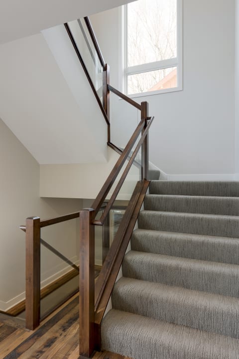 A contemporary staircase with a wooden bannister and gray carpet.