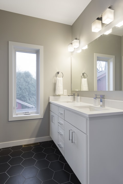 Modern bathroom interior with a white vanity, double sink, and hexagonal black tiles on the floor.