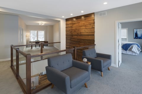 A contemporary living area featuring gray armchairs, a wooden accent wall, and a view into a cozy bedroom.