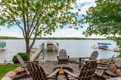 Lakeside view with Adirondack chairs, fire pit, and boat dock.