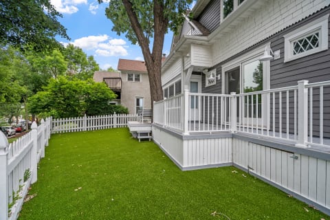 A yard with artificial grass, white picket fence, and a stylish house.
